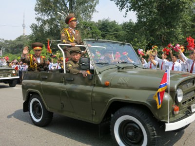 Military vehicles drive past with lots of North Korean army guys, all proudly dressed and happy.